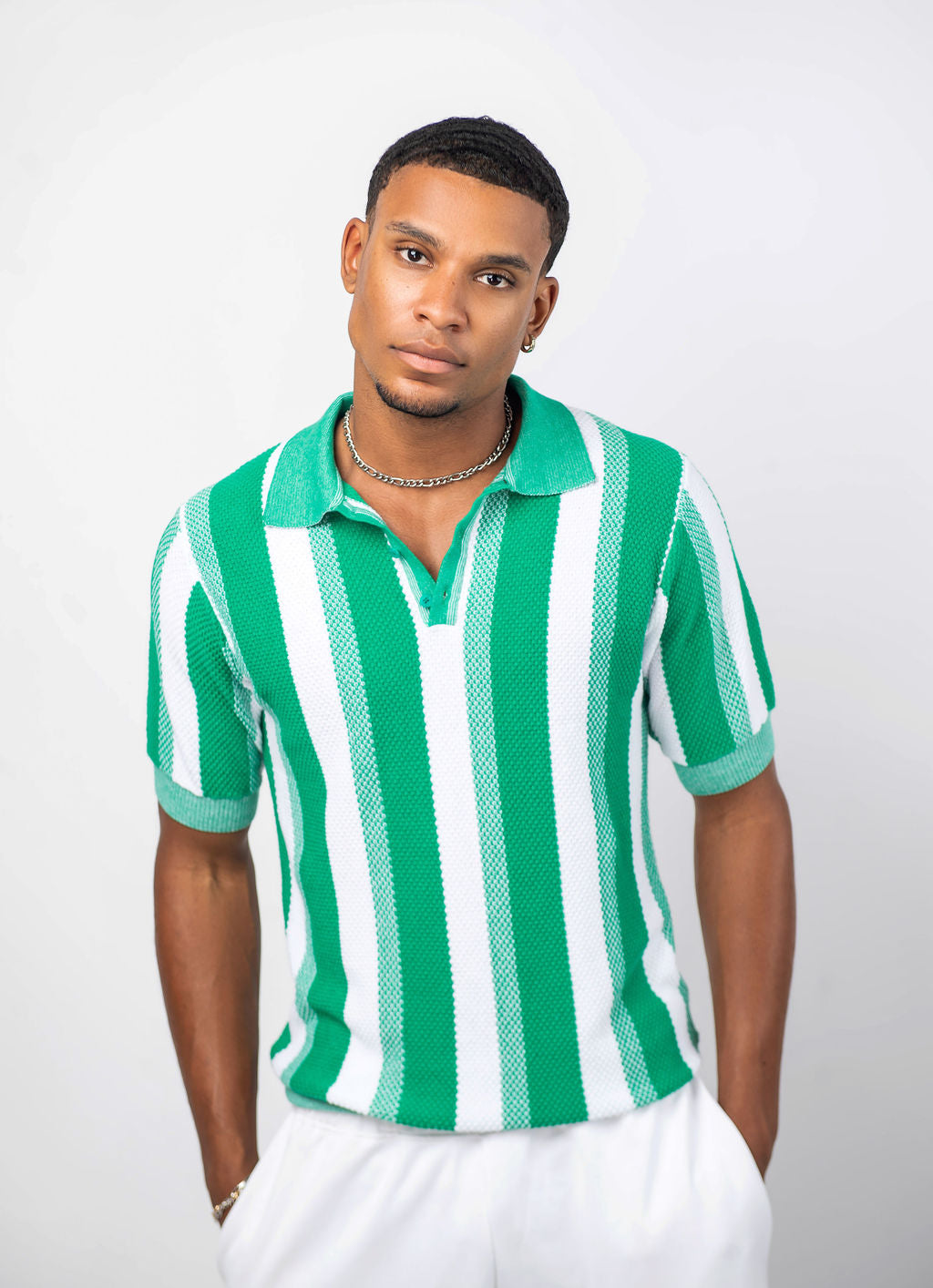 A man wearing a green and white striped knit shirt with a collar, paired with white trousers.