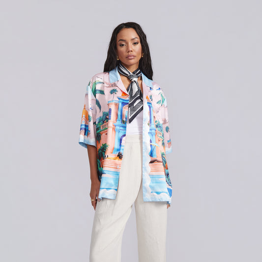Woman wearing a colorful patterned shirt and white pants on a gray background