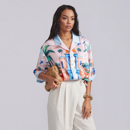 Woman wearing a colorful patterned shirt with a plain background. Shirt inspired by travel, holiday and resort lifestyle