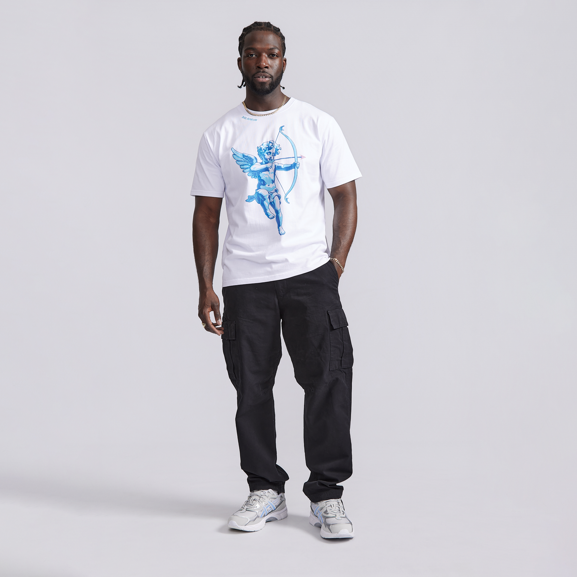 Man wearing a white t-shirt with a graphic design and black cargo pants on a light gray background