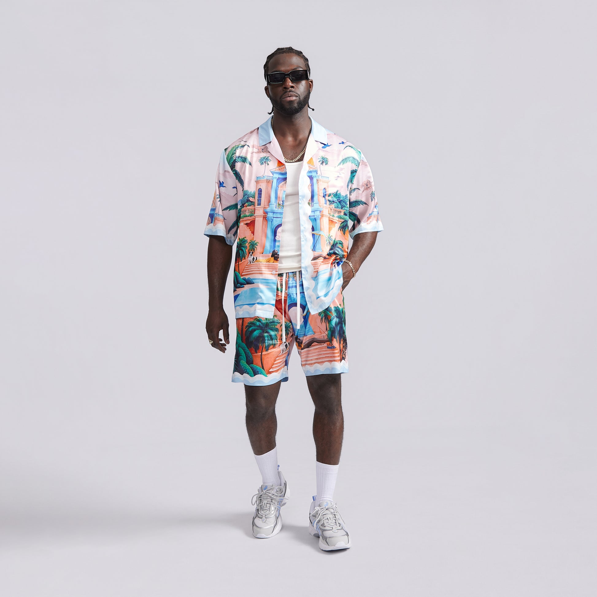 Man wearing a colorful tropical shirt and shorts set on a gray background