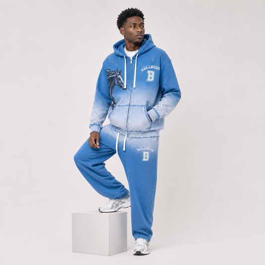 A man models a blue zip-up hoodie and matching sweatpants set with a white gradient fade, featuring a wolf graphic and 'BALADEUR' branding, posed on a light gray studio background.