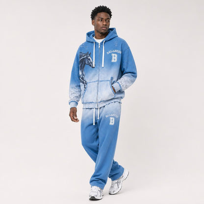 A man modeling a blue zip-up hoodie and matching sweatpants set with a faded gradient wash, featuring a horse graphic on the hoodie chest, white drawstrings, and 'BALADEUR' with a 'B' logo on the front and pants.