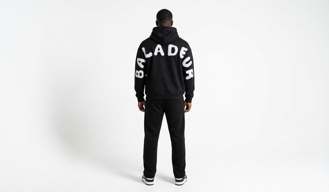 Person wearing a black tracksuit with 'Baladeur' branding on a white background
